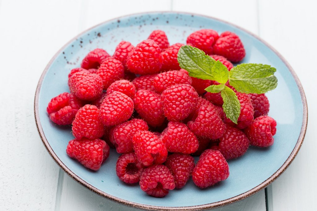 Fresh raspberries in a plate on a vintage background.